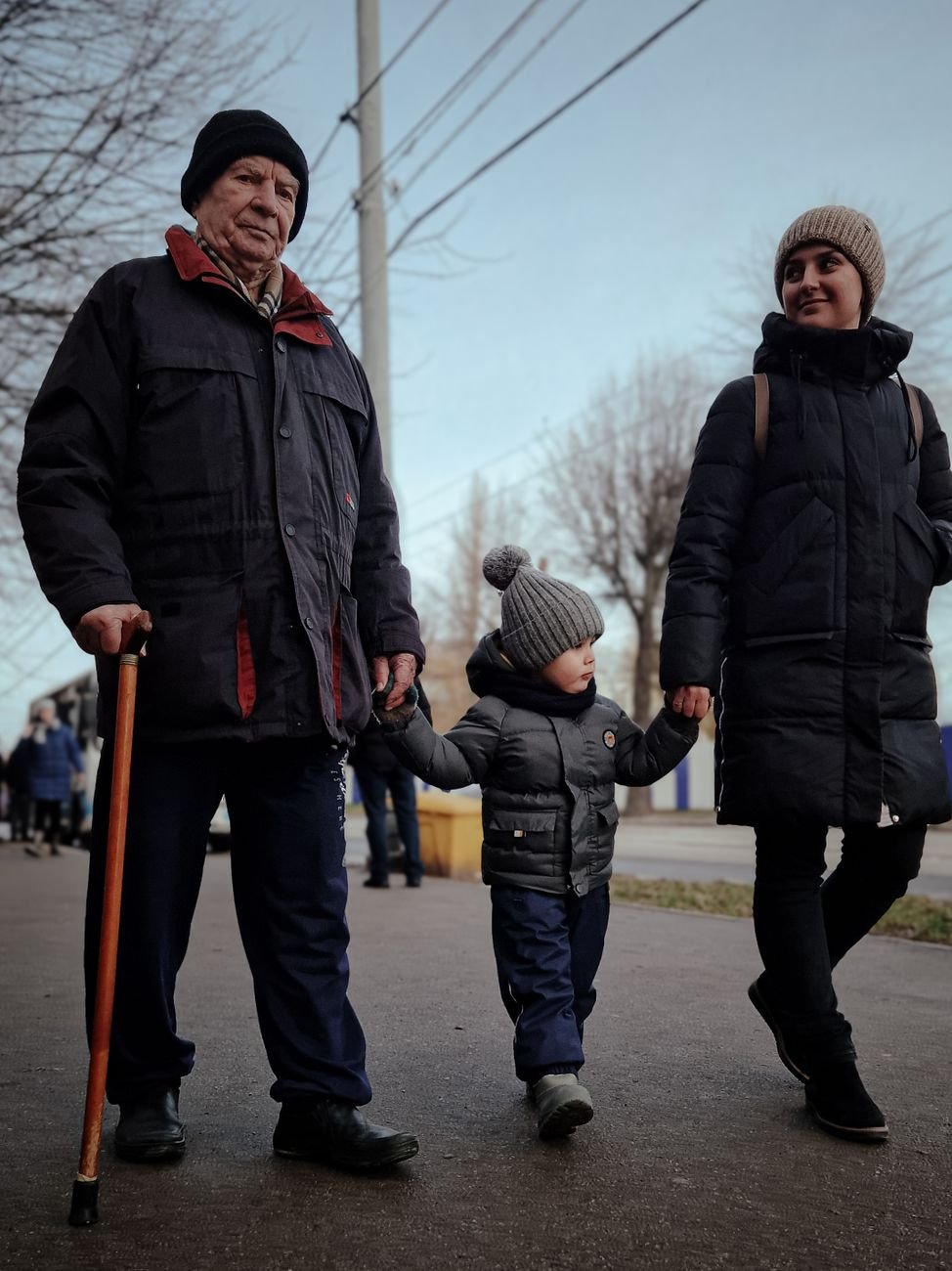 Grandfather, mother, and child walking outdoors on a chilly day.